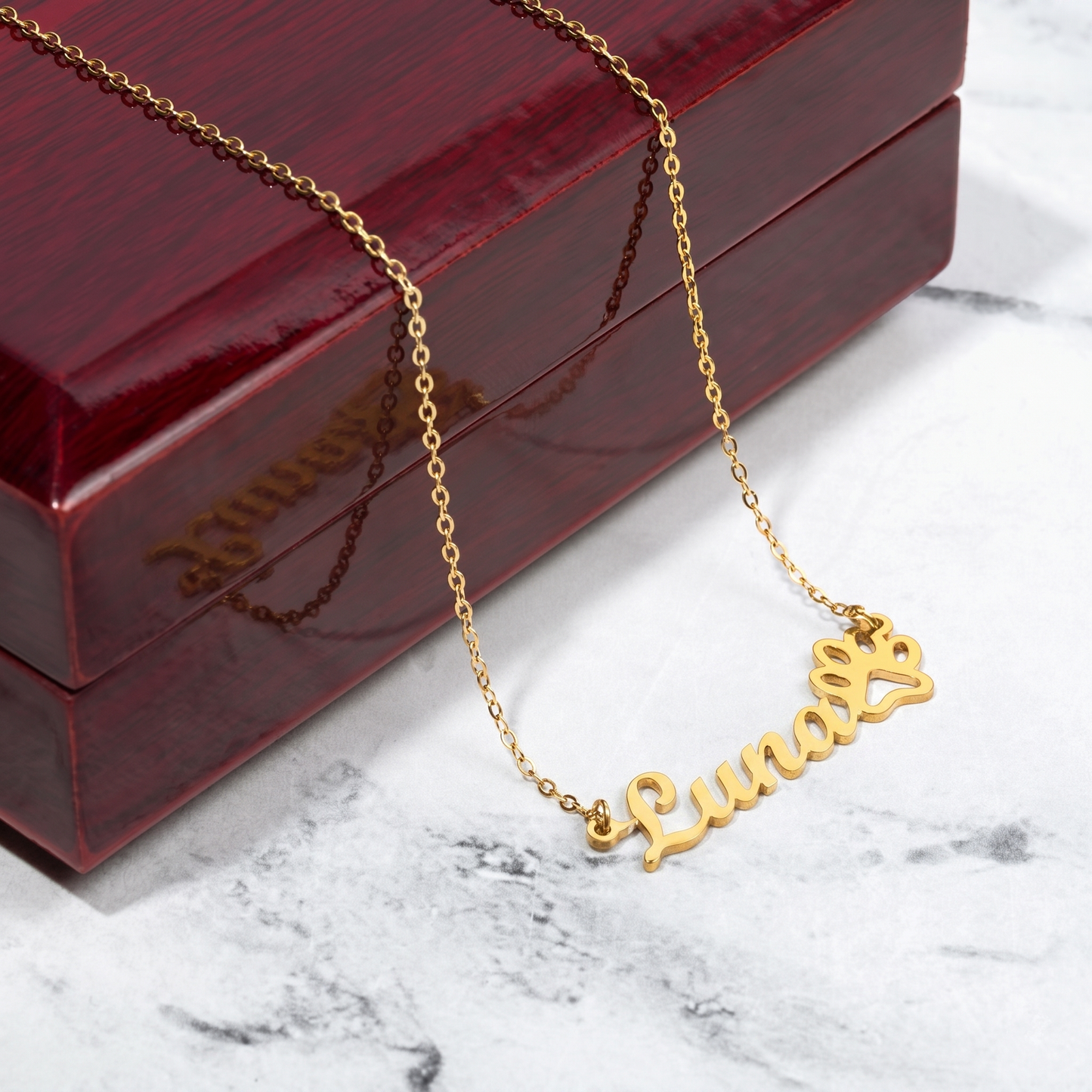 Gold necklace with 'Luna' pendant on a marble surface with a red jewelry box.