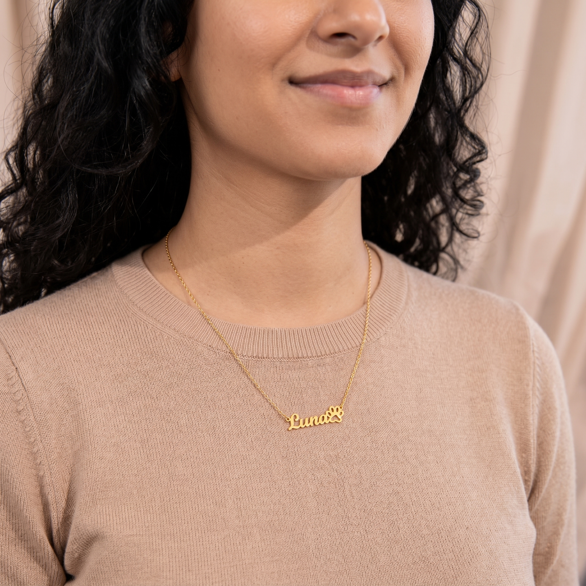 Woman wearing a gold necklace with 'Luna' engraved on it against a neutral background