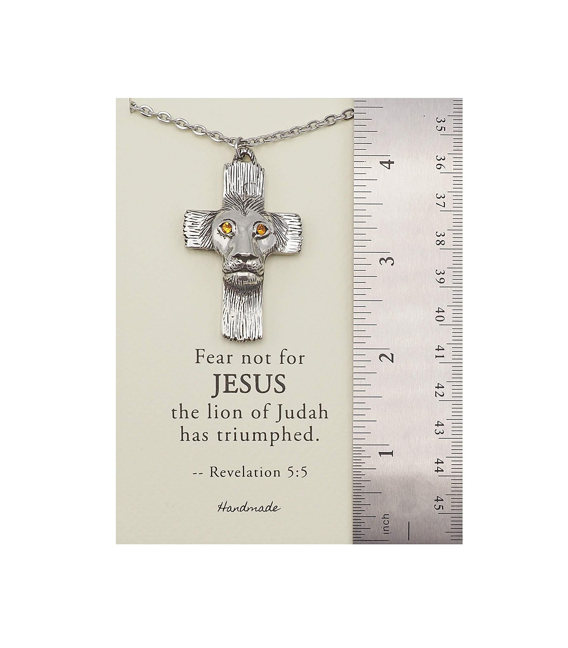Silver cross necklace with lion head design on a card with text, next to a ruler for scale.