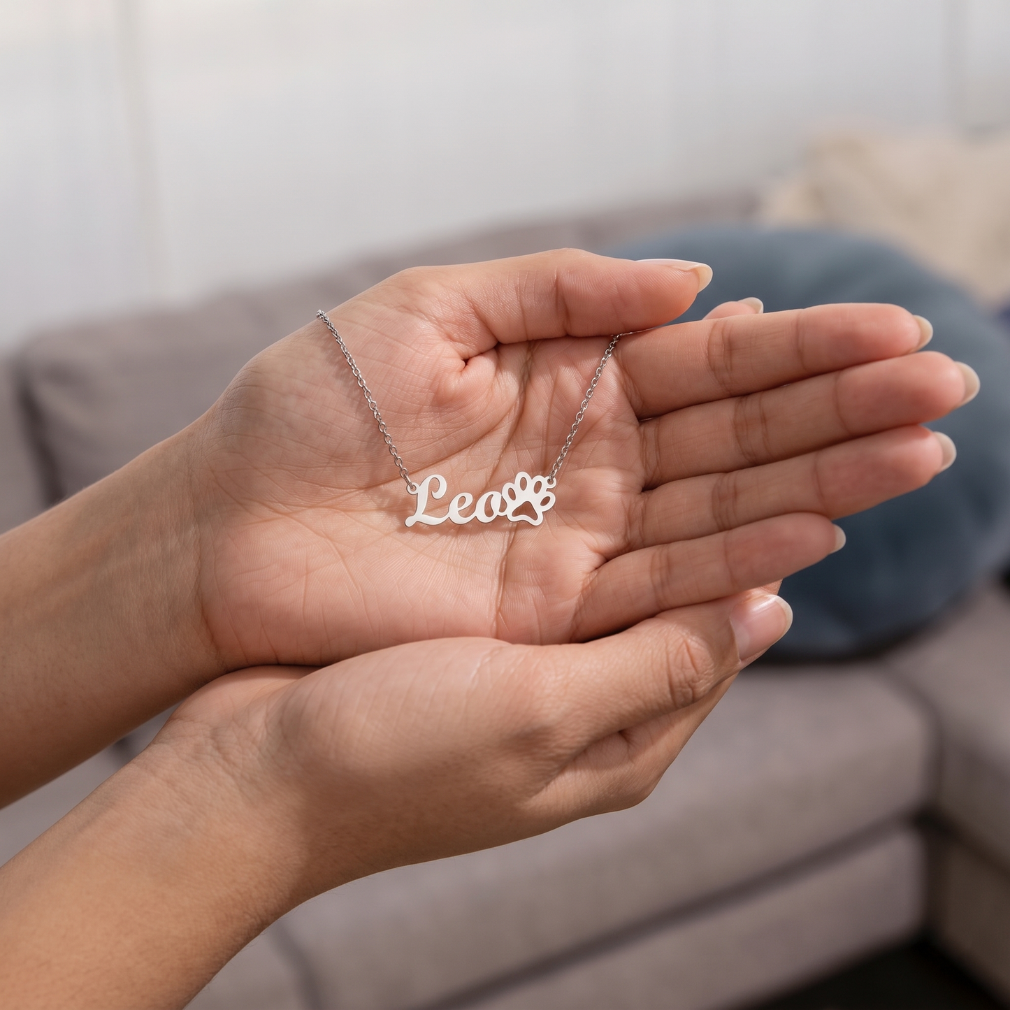 Person holding a silver necklace with 'Lea' on a neutral background