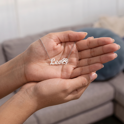 Person holding a silver necklace with 'Lea' on a neutral background