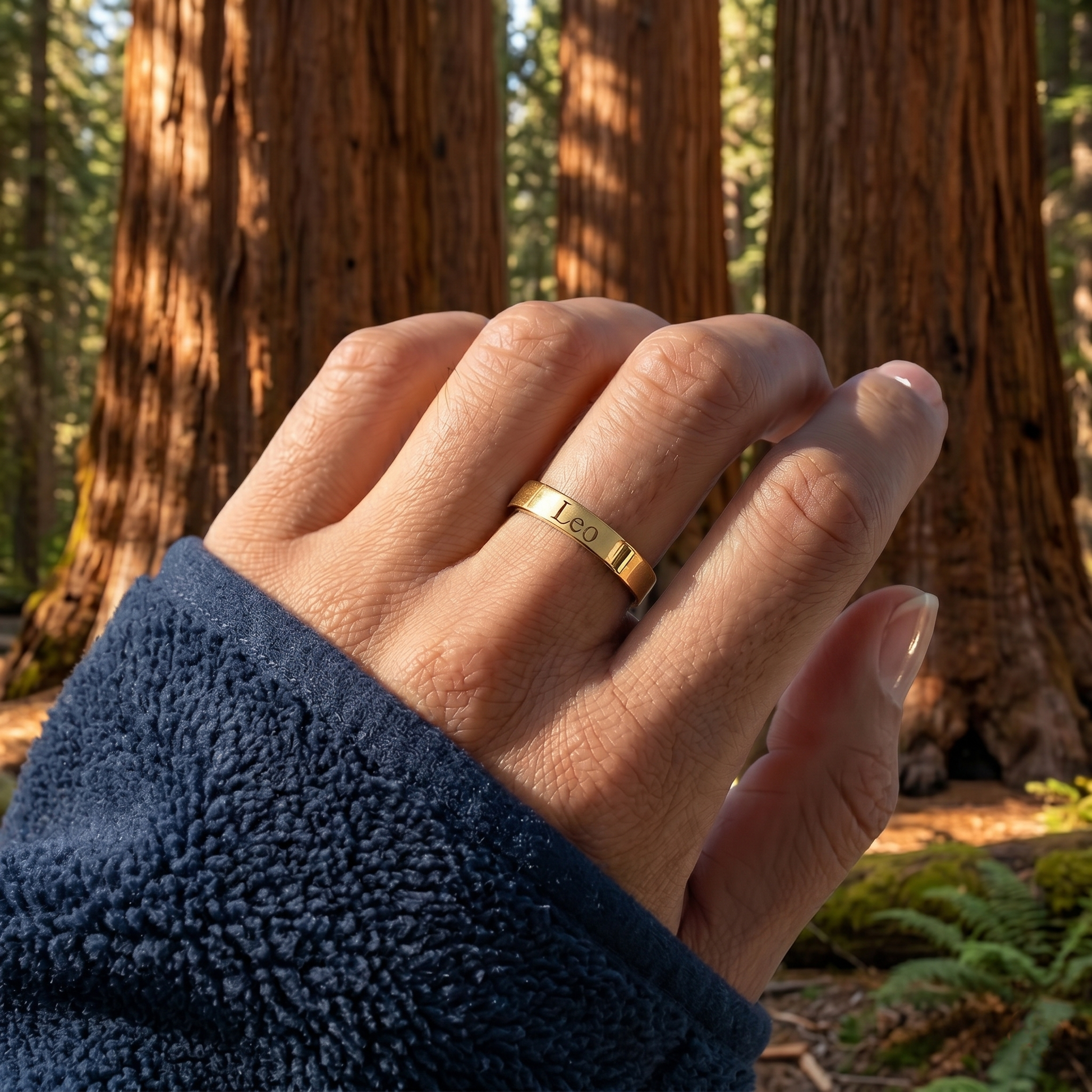 Hand wearing a gold ring with 'LOVE' engraved, set against a forest background