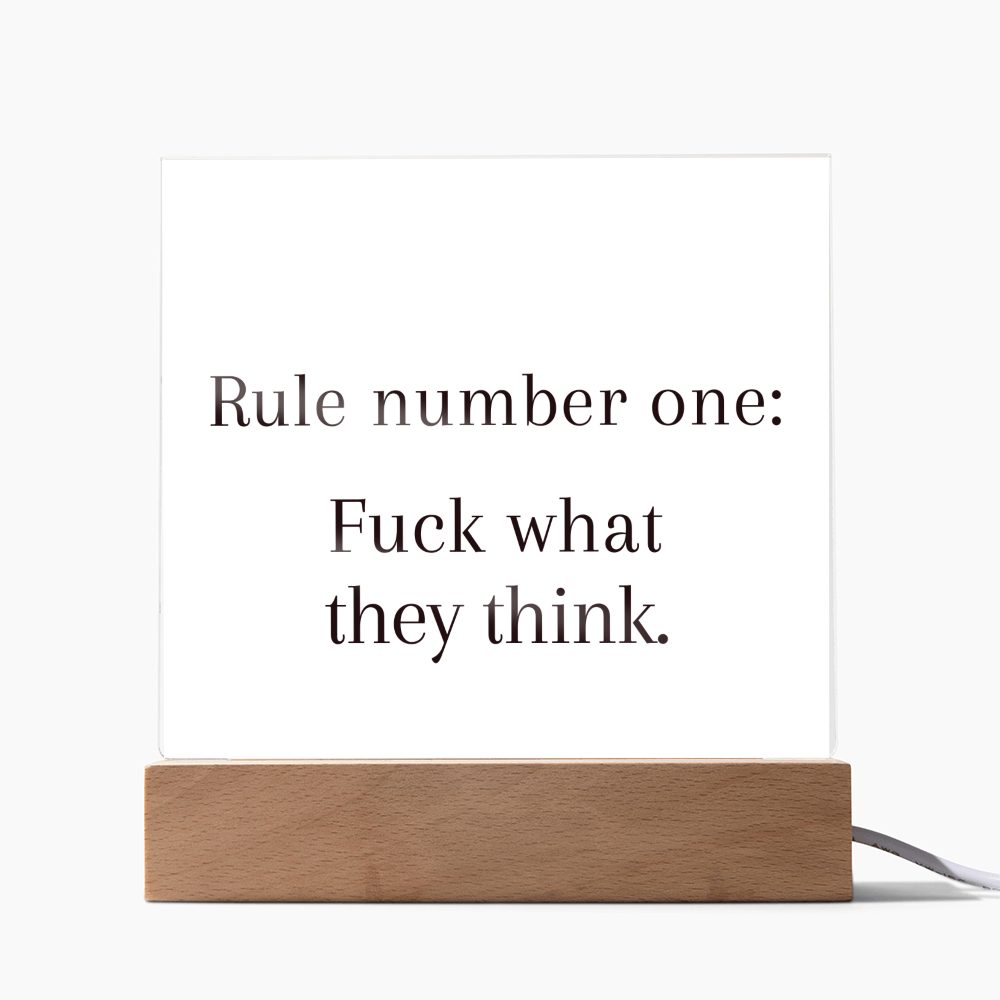 Acrylic plaque with quote “Rule Number One: F*ck What They Think” glowing on LED wooden base.