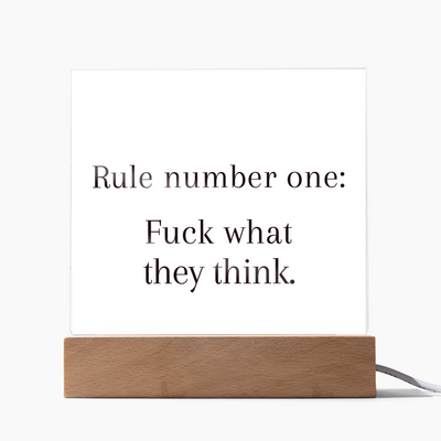 Acrylic plaque with quote “Rule Number One: F*ck What They Think” glowing on LED wooden base.