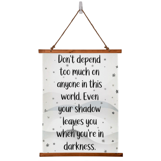 Wood framed quote tapestry reading ‘Don’t depend too much on anyone…’ hanging on wall