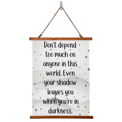 Wood framed quote tapestry reading ‘Don’t depend too much on anyone…’ hanging on wall