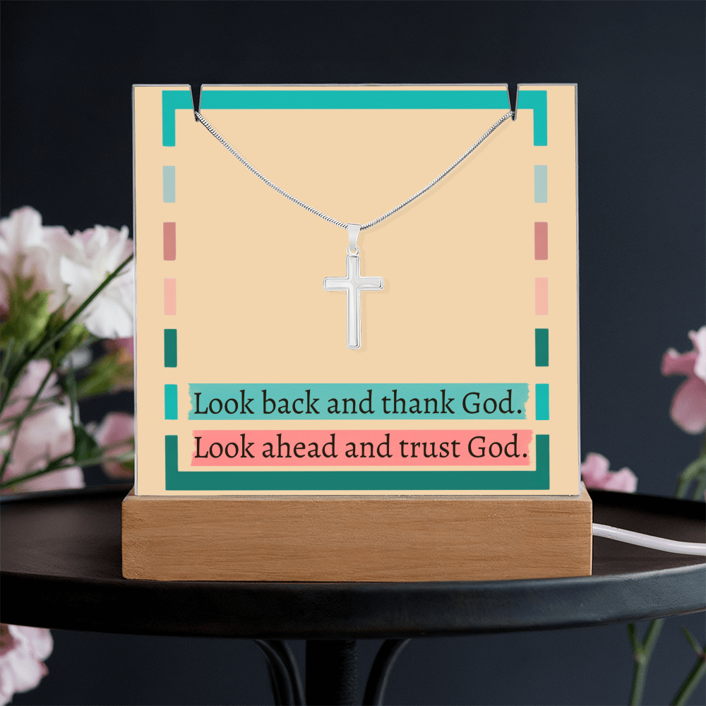 Stainless steel cross pendant on snake chain beside acrylic display